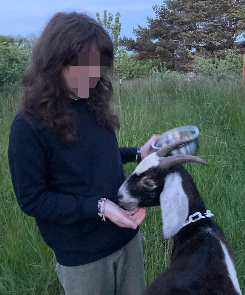 The author on a farm with food in her hand feeding a goat